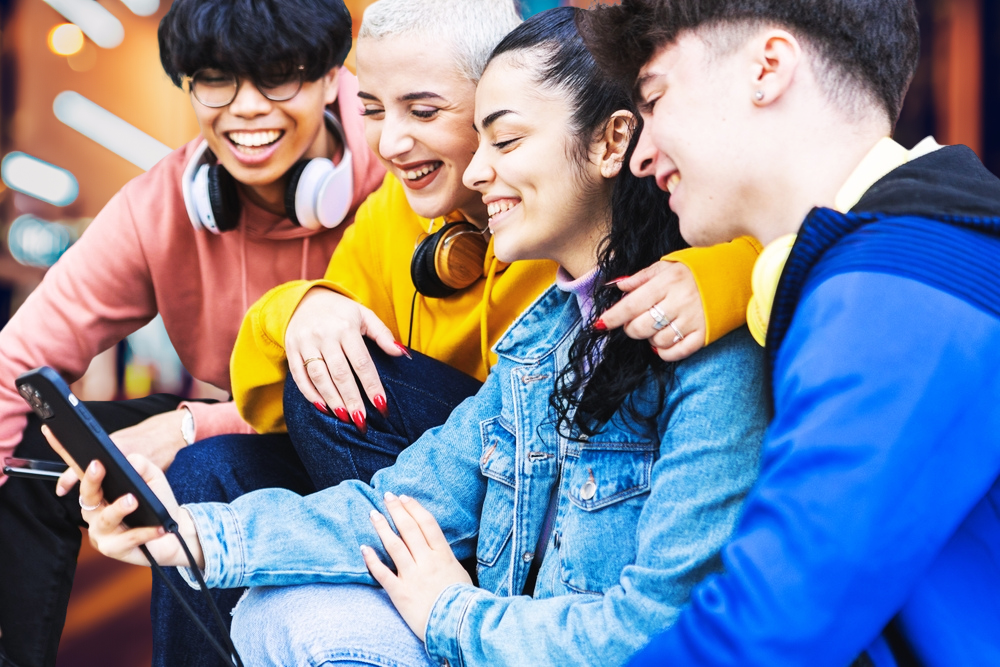 Four Gen Z travelers watching a travel video on the middle girl's phone.