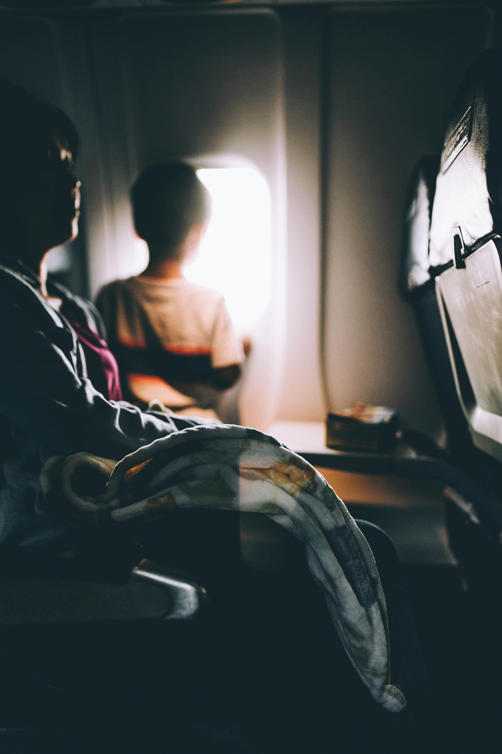 Mom traveling on a plane with a small child who is watching the clouds through the window.